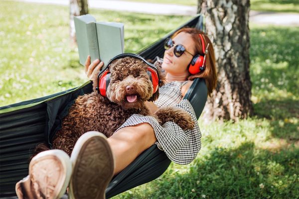 Frau liegt mit Hund in Hängematte. Beide haben Gehörschutz auf.